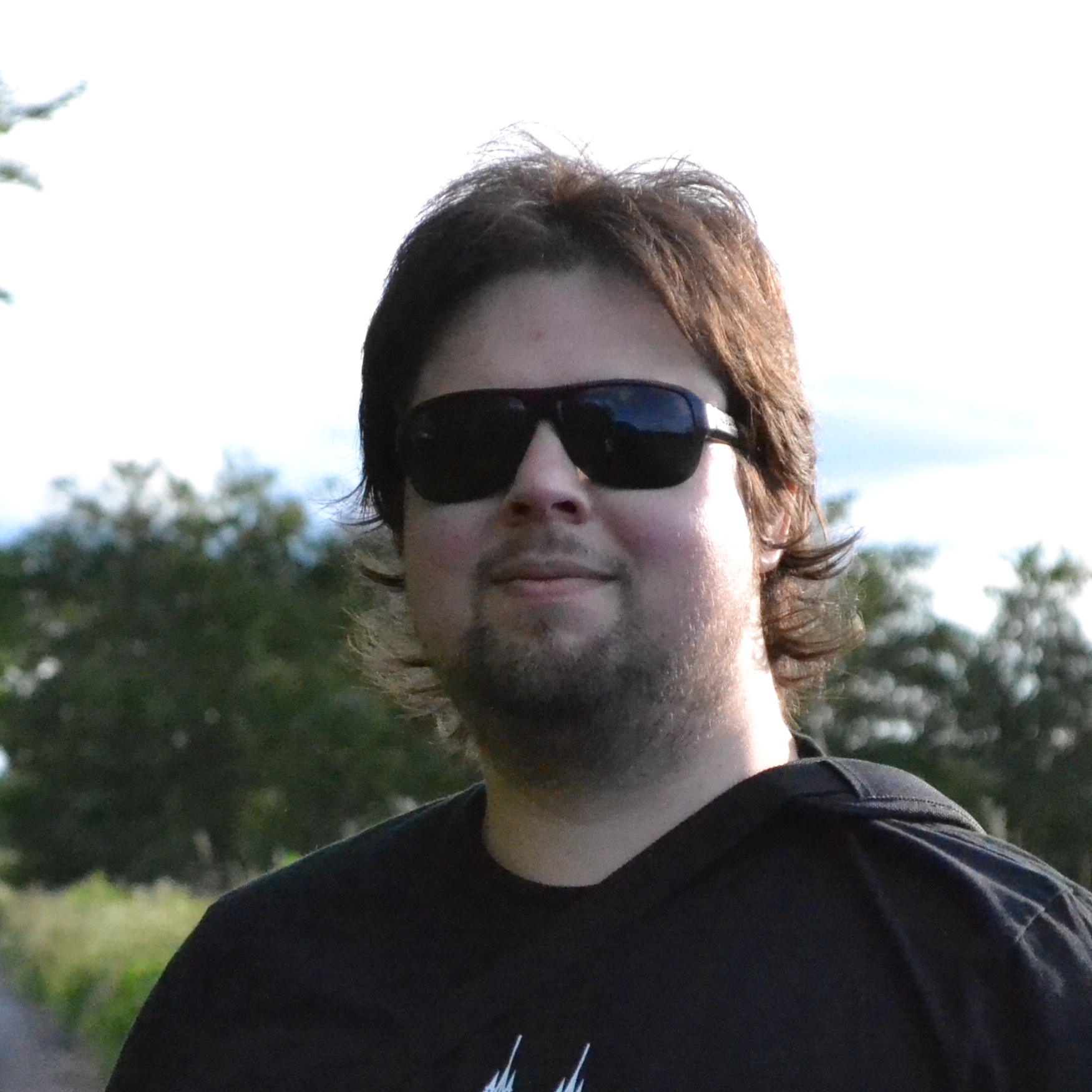 Profile picture: irl wearing a black t-shirt and sunglasses. He is outdoors and the weather is nice.